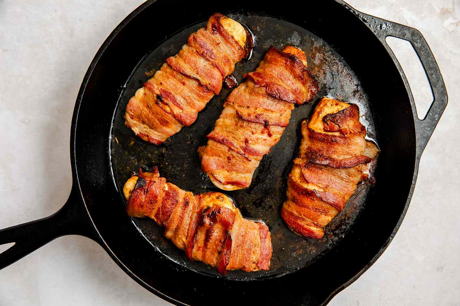Bacon-Wrapped Chicken cooking in a large cast iron skillet