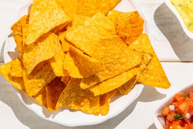 A plate of tortilla chips next to bowls of dip and salsa