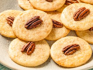 Closeup view of a beige platter of sand tart cookies topped with a pecan halves resting on a green napkin
