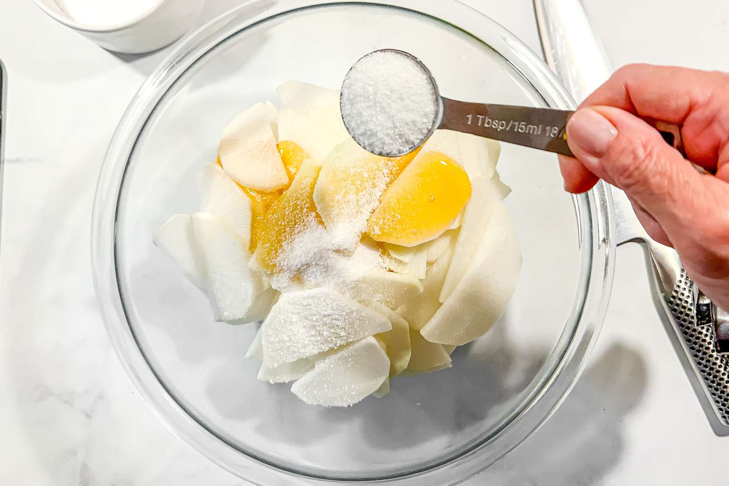 Tablespoon of Salt Added to a Bowl of Sliced Korean Radish Topped With Honey, and in the Surroundings, a Knife and a Bowl of Salt for Mul Naengmyeon Recipe