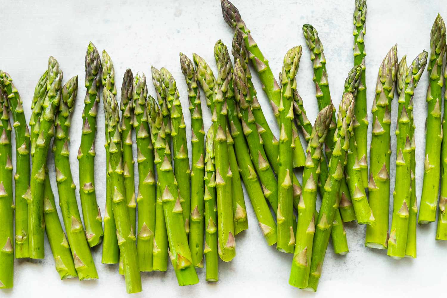 Close up of fresh bright green asparagus on white parchment paper