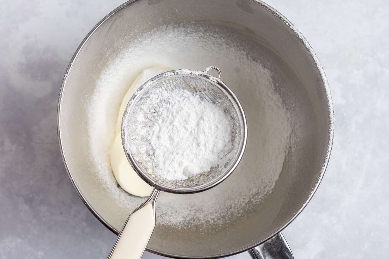 Sifting powdered sugar into a mixer bowl to make an easy no bake cheesecake recipe.