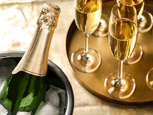 Champagne bottle in an ice bucket next to a tray with filled champagne flutes