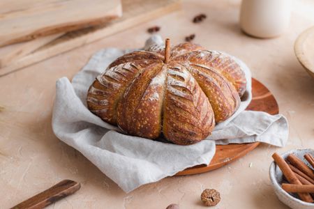 Pumpkin-shaped sourdough on a grey linen with cinnamon sticks next to it.
