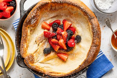 A Dutch Baby pancake topped with fresh strawberries, blackberries, and powdered sugar displayed in a skillet