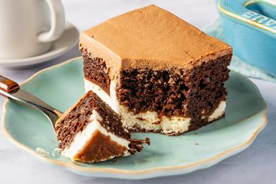 A piece of layered chocolate cake with cream filling and chocolate frosting on a plate, with a fork beside it