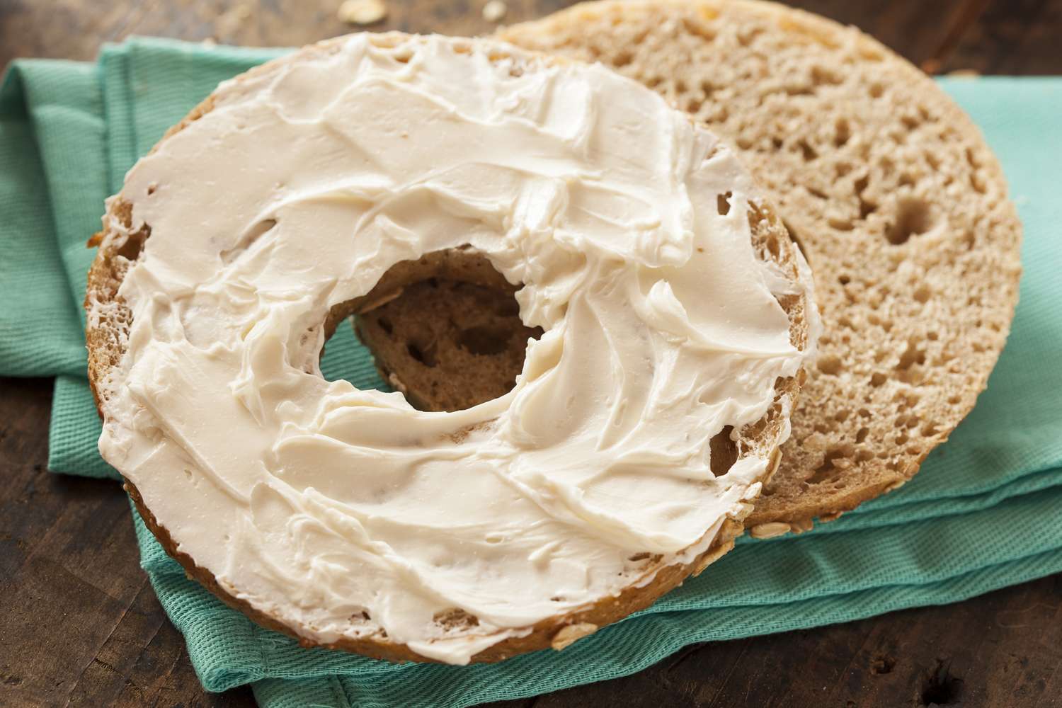 A bagel half spread with cream cheese on a turquoise fabric surface