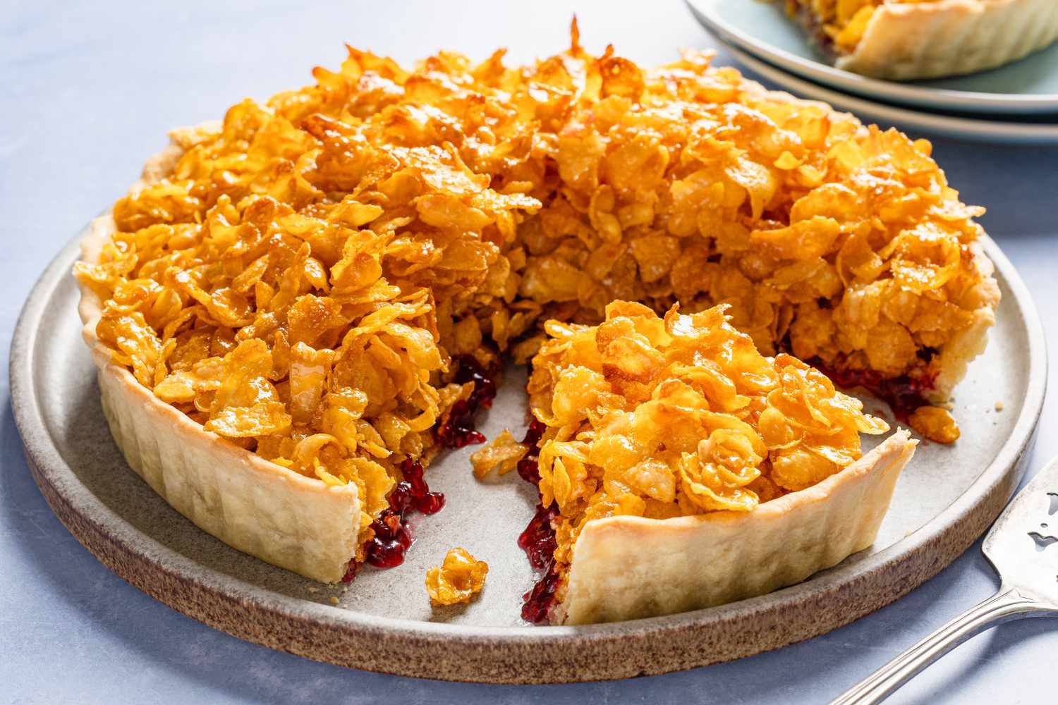Cornflake tart (part of it sliced and missing a piece) on a plate and in the background, a slice on a small plate