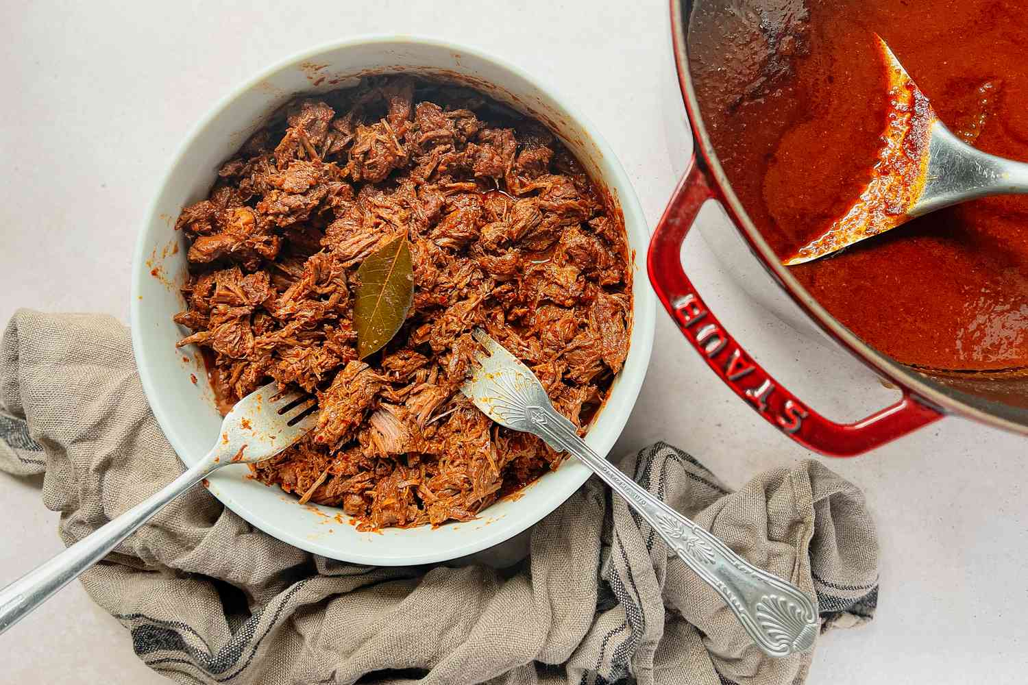 Cooked beef being shred in a bowl with two forks