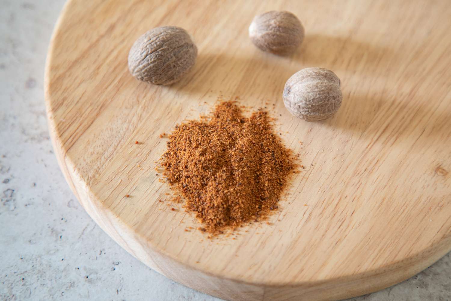Pile of ground nutmeg next to three whole nutmegs
