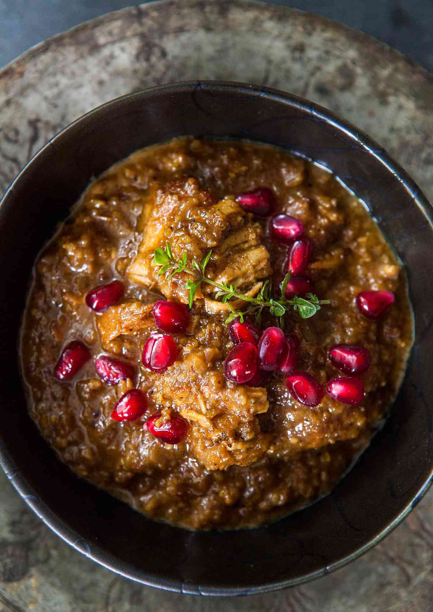 A bowl of chicken stew garnished with pomegranate seeds and herbs