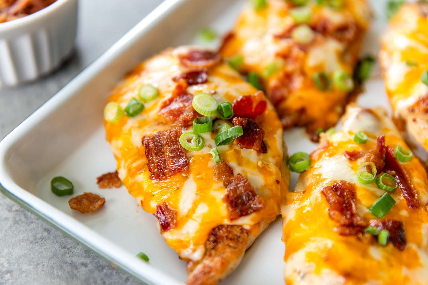 Cooked chicken breasts topped with bacon, cheese, and green onions in a baking dish