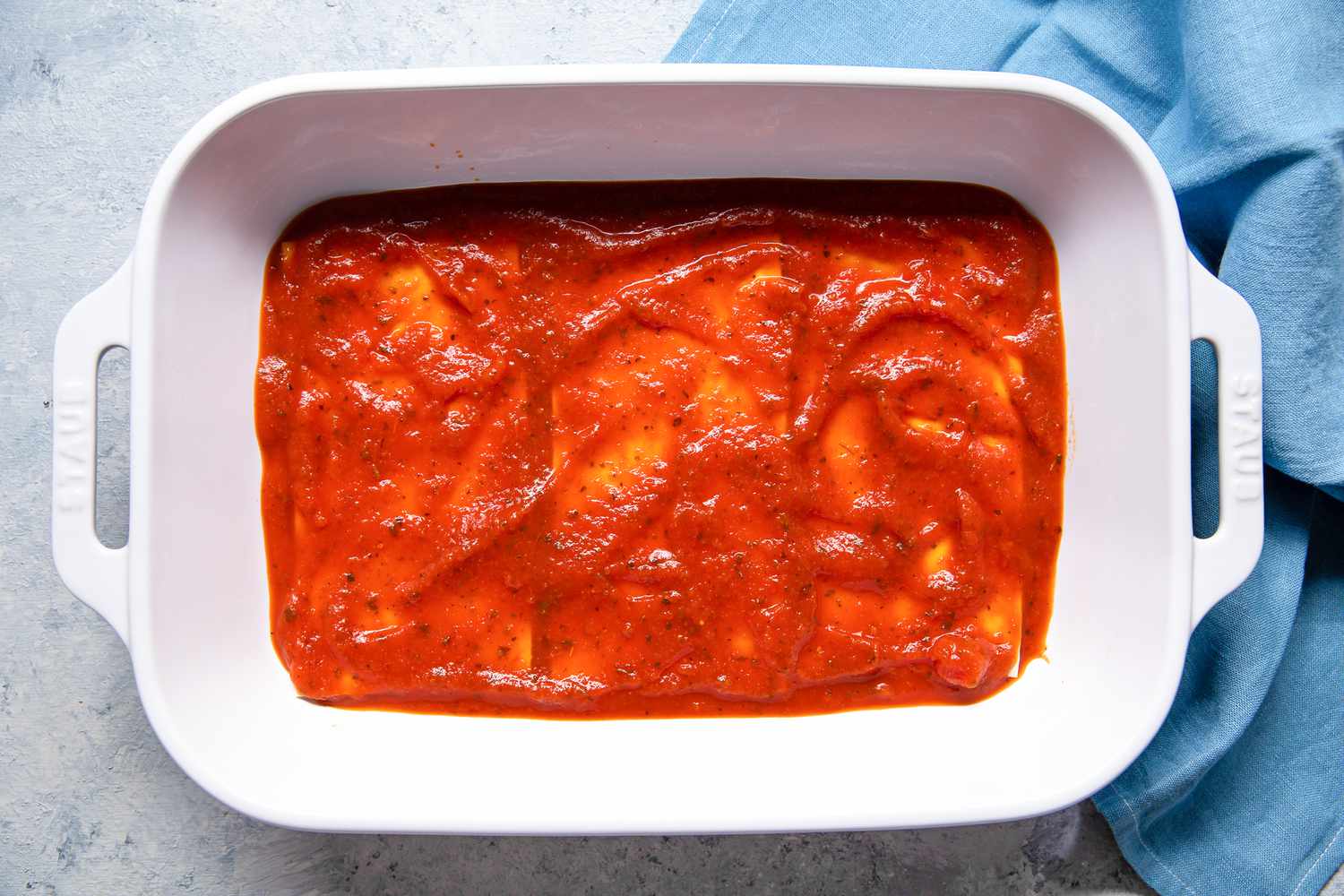 Another Layer of Marinara Sauce Added in the Casserole Dish Next to the Sky Blue Kitchen Towel for Pepperoni Pizza Lasagna