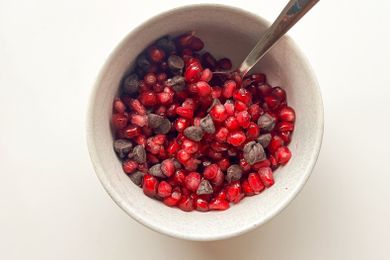 A bowl containing pomegranate seeds and chocolate chips with a spoon