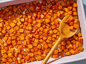 Small cubes of sweet potato, roasted in a baking pan, with a wooden swerving spoon scooping some potato cubes up