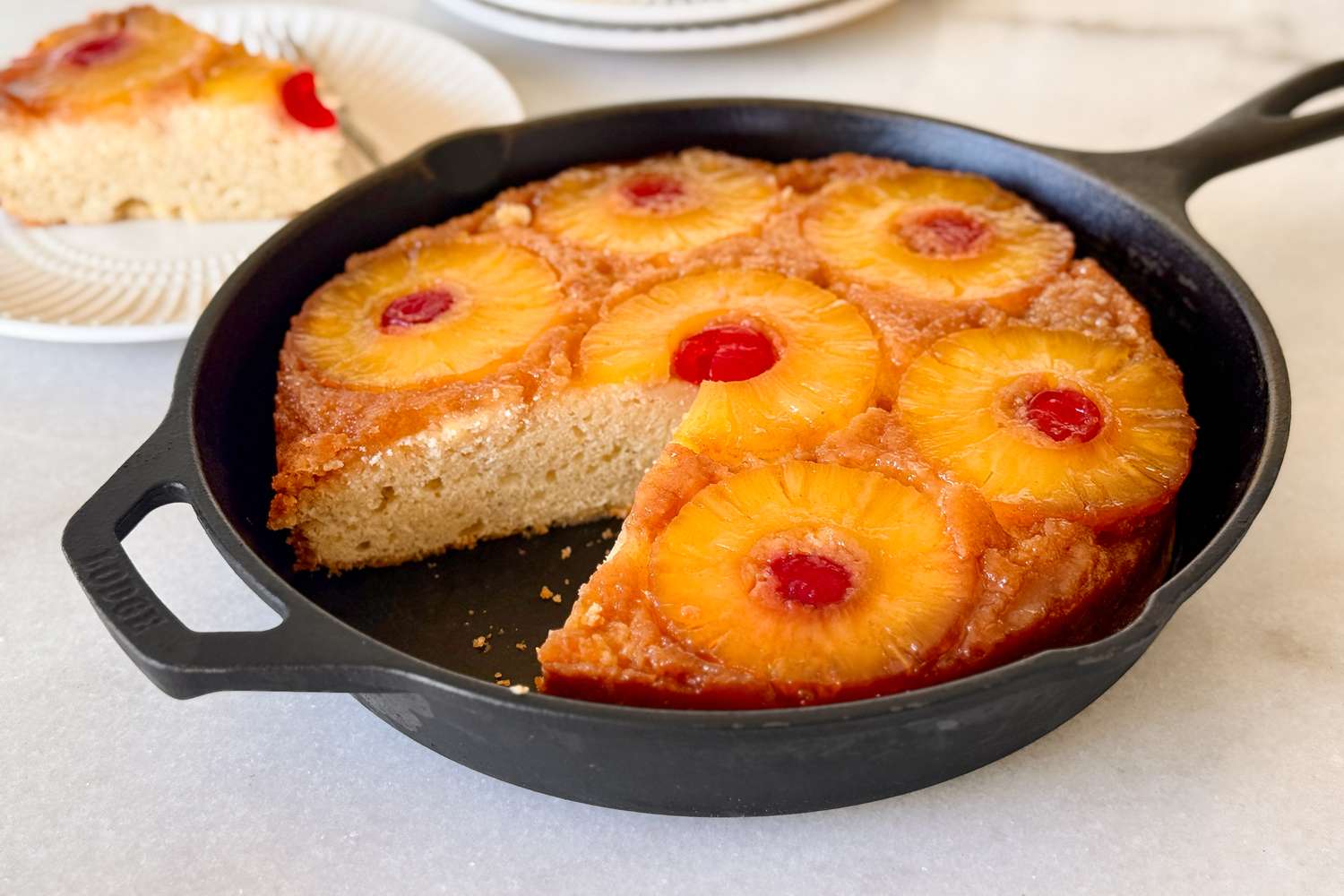 A pineapple upsidedown cake in a cast iron skillet with one slice removed