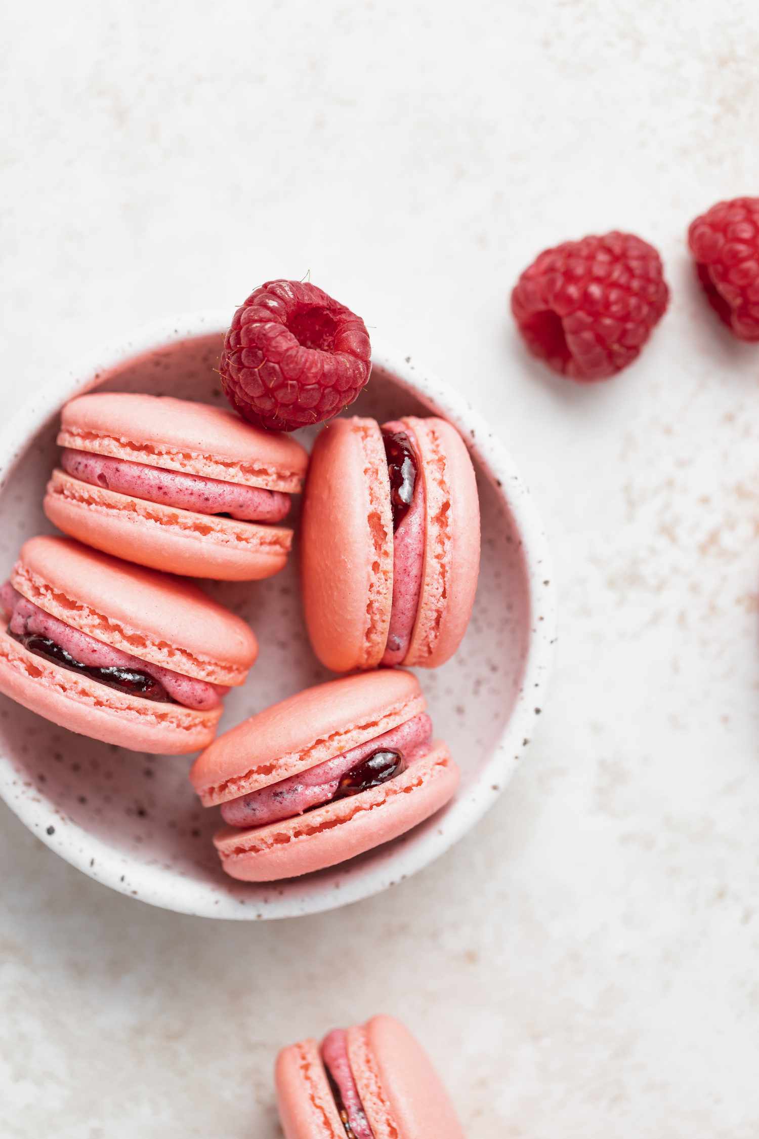 Overhead view of raspberry macarons filled with raspberry buttercream in a small bowl.