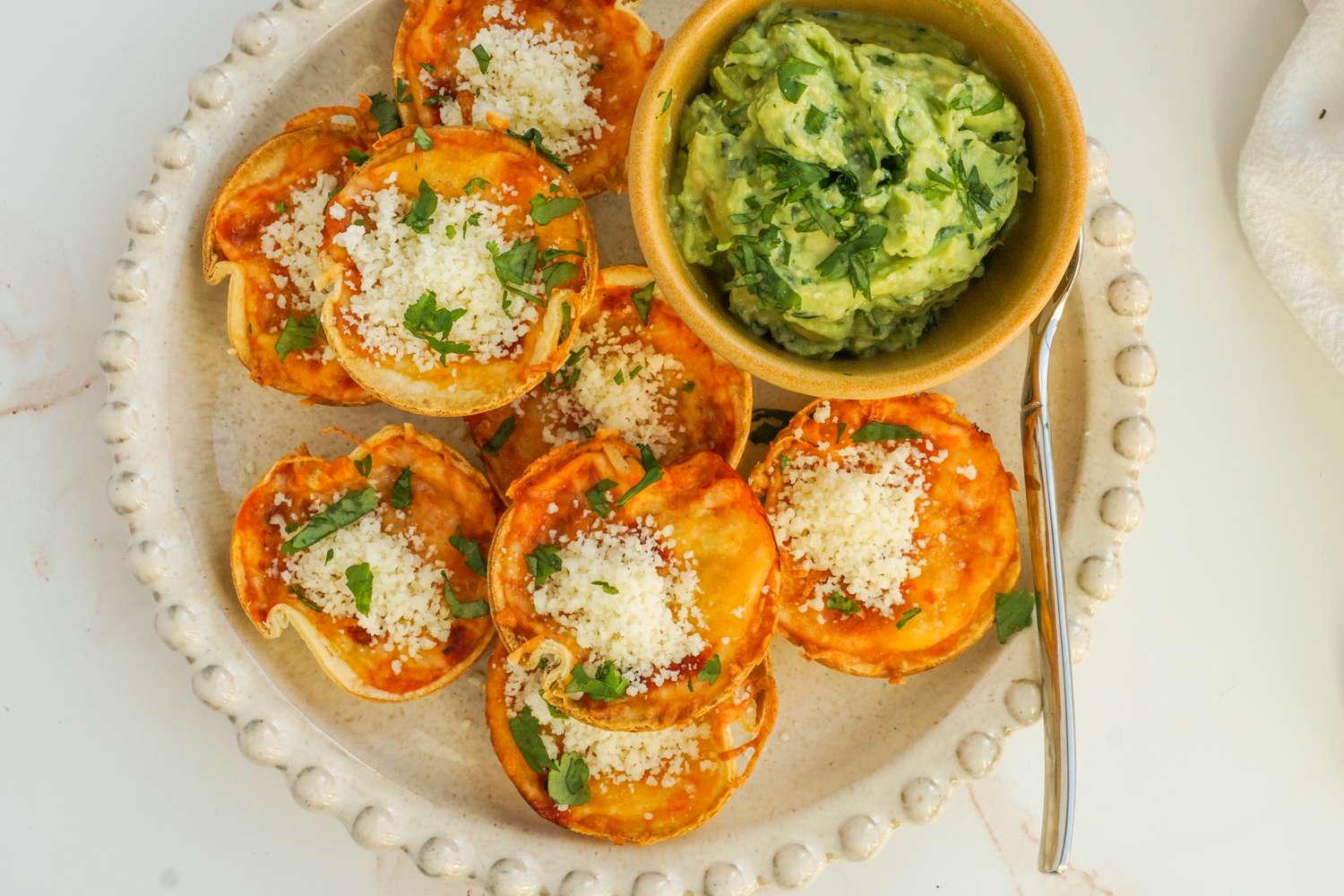A plate of enchilada bites accompanied by a bowl of guacamole