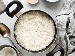 Overhead view of pot of white rice on a counter next to a serving spoon and a gray towel