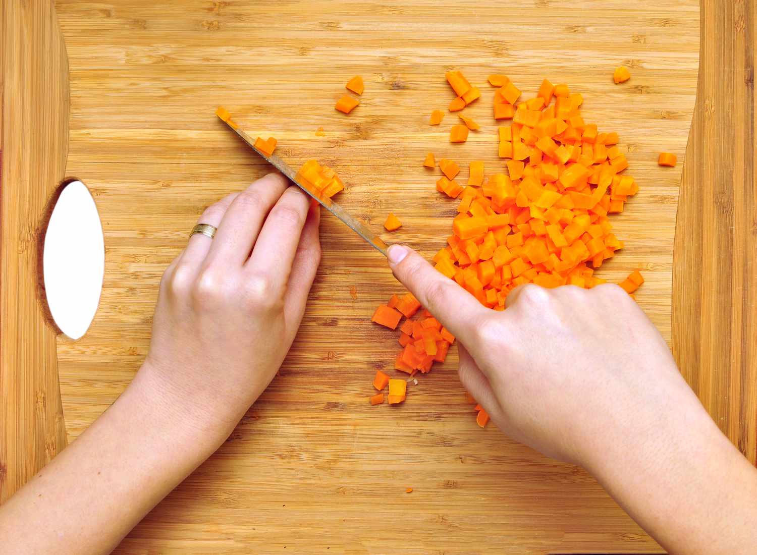 Hands dicing carrots on a bamboo cutting board