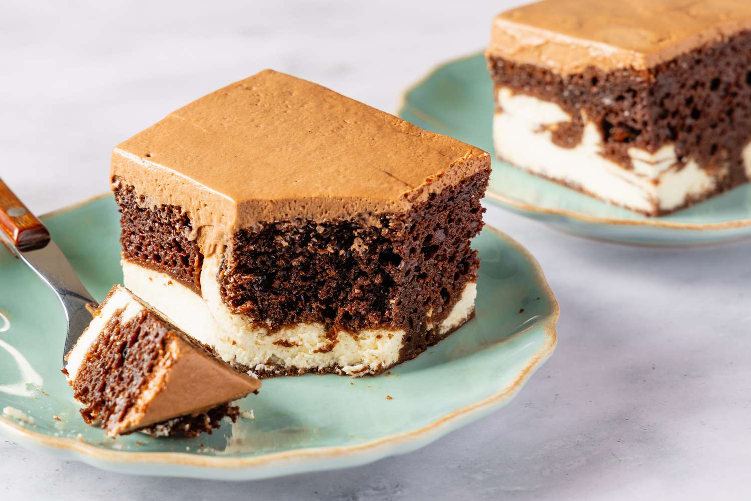 A slice of chocolate cake with a creamy filling on a green plate, a fork with a piece