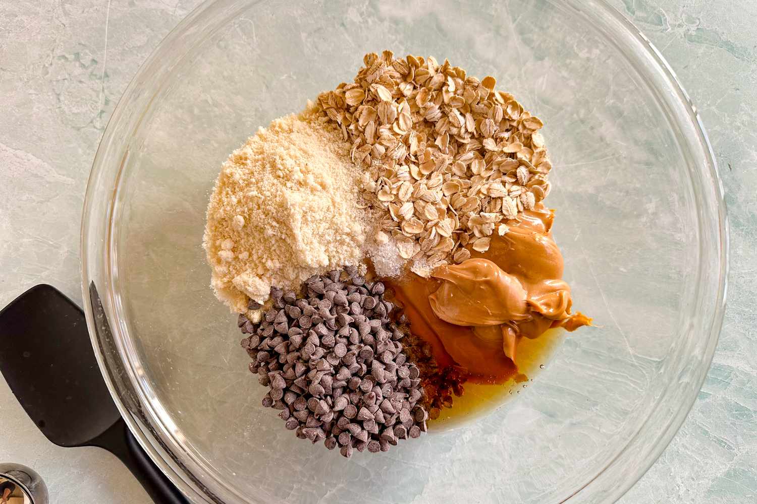 Overhead view of a large clear glass mixing bowl with ingredients for energy balls before mixing