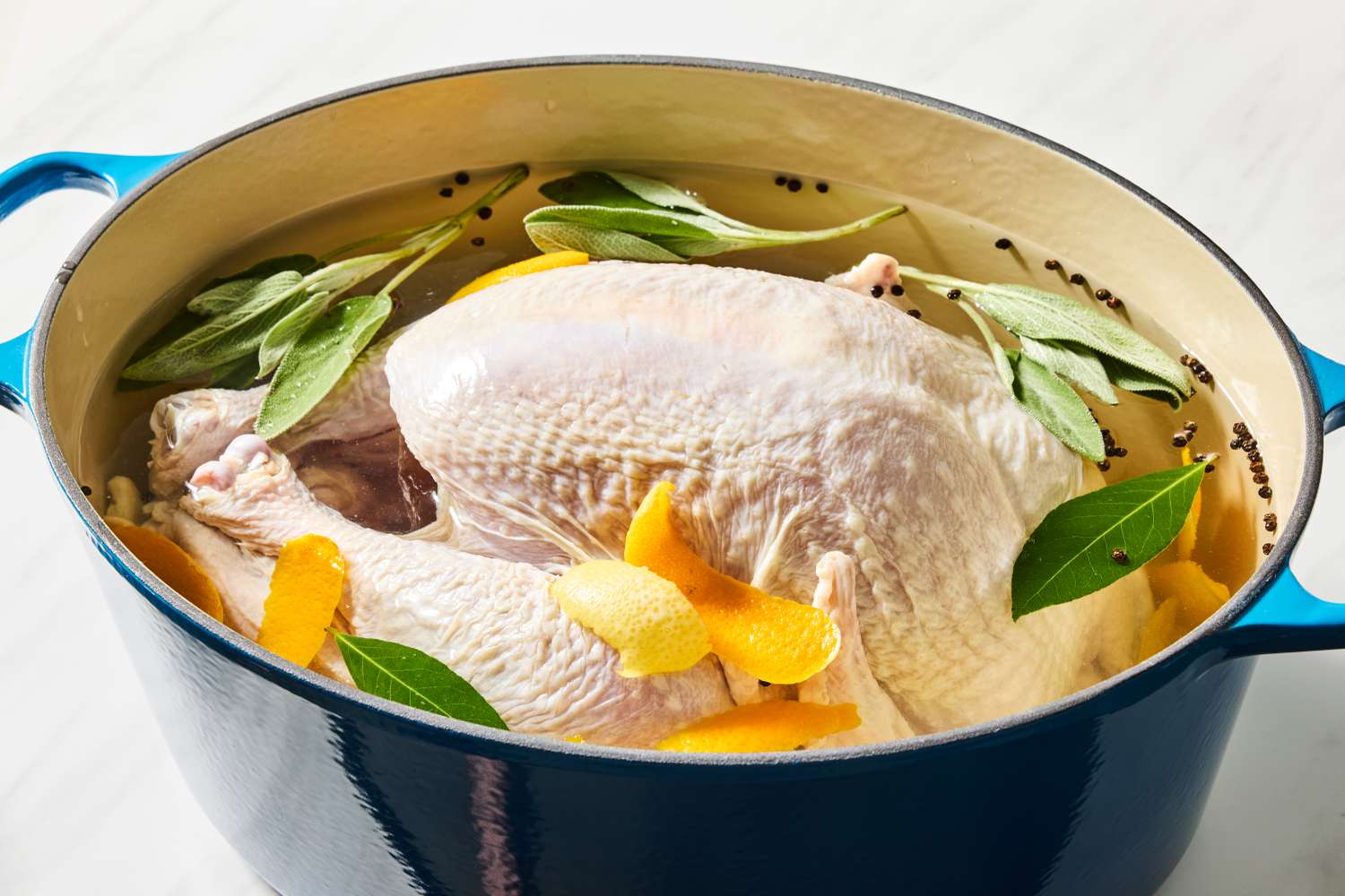Raw turkey in a pot of brine with orange zest, sage, and bay leaves