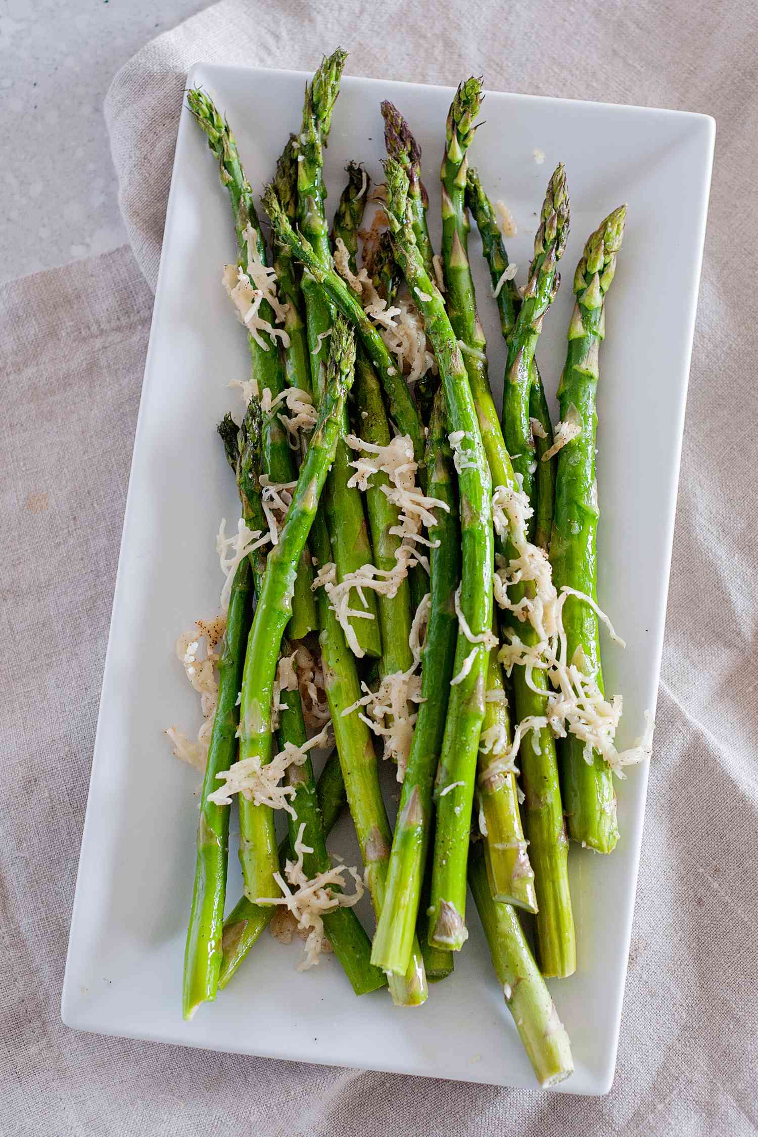 A white platter of oven roasted asparagus with Parmesan