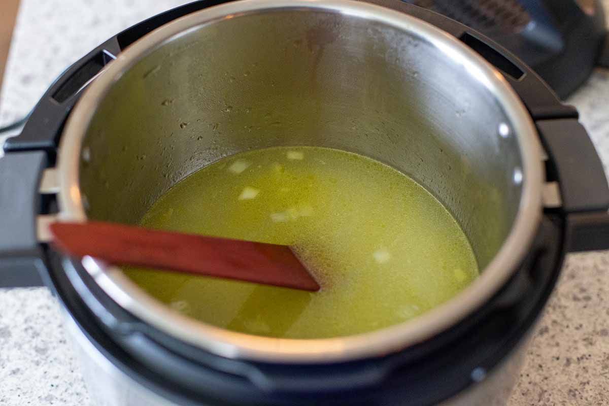 Inside of an instant pot with a green broth for the best instant pot chicken tortilla soup. A wooden spoon is also inside the pot.