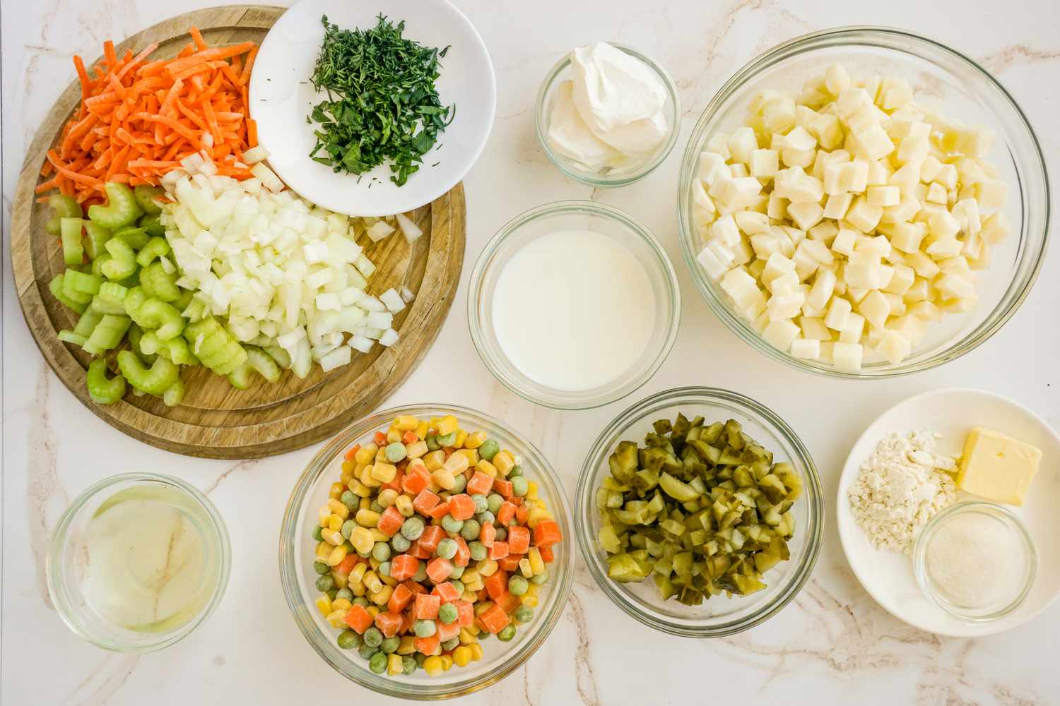 Ingredients for a soup including chopped vegetables diced potatoes and seasonings displayed in bowls on a countertop