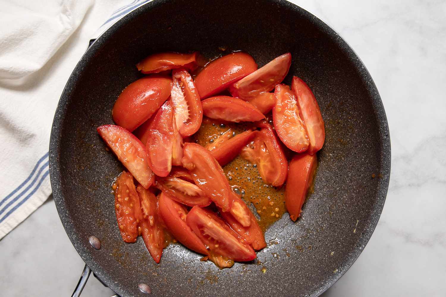Tomato wedges just starting to soften as they cook in a skillet