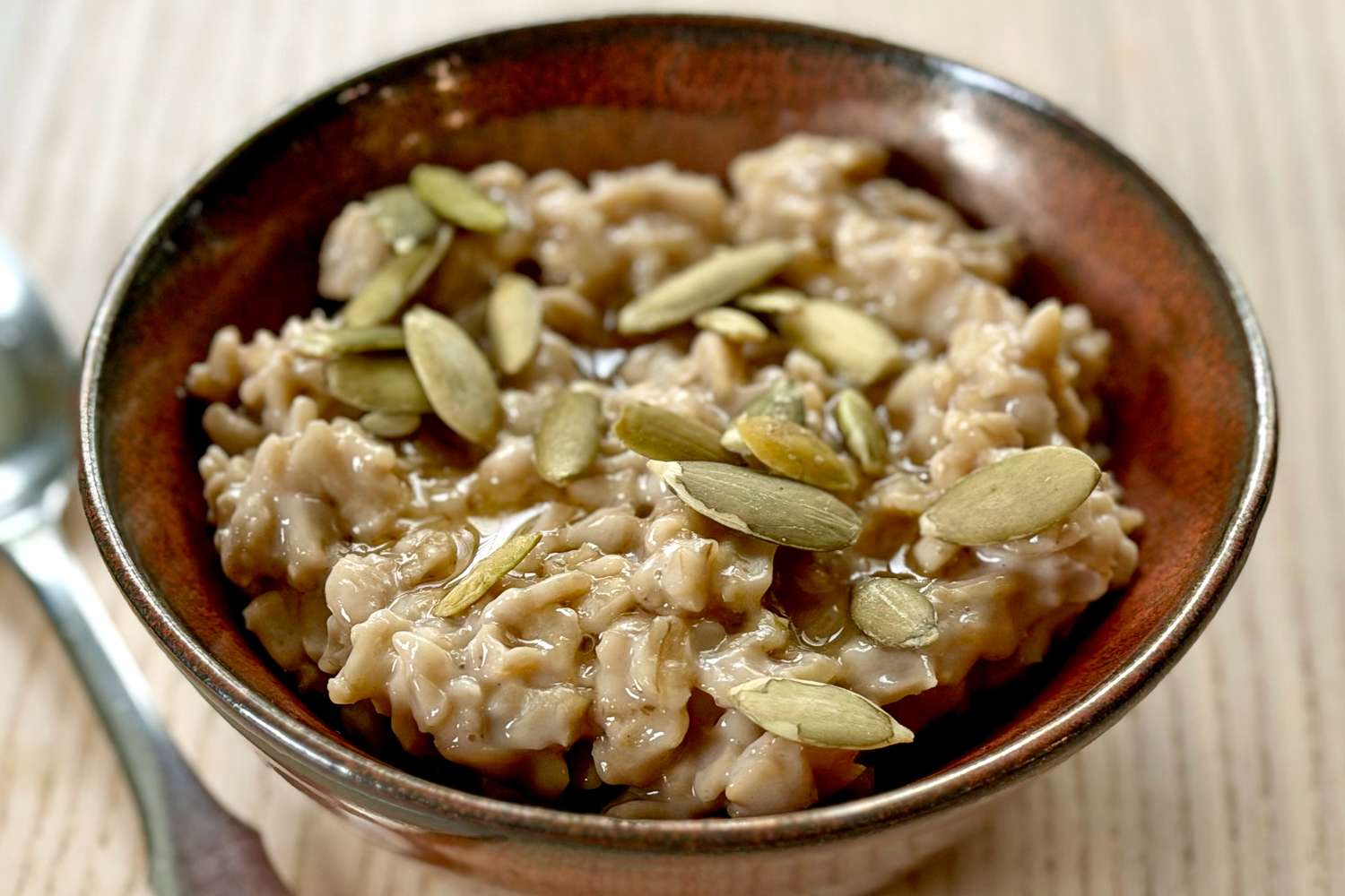 A bowl of oatmeal topped with pumpkin seeds on a wooden table