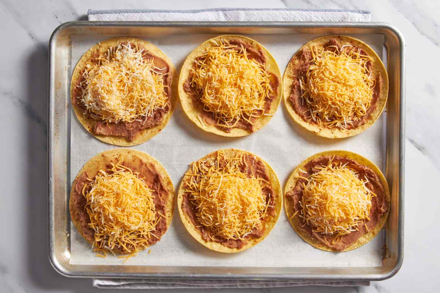 Shredded cheese added to toasted tacos on a baking sheet for cheesy baked taco recipe