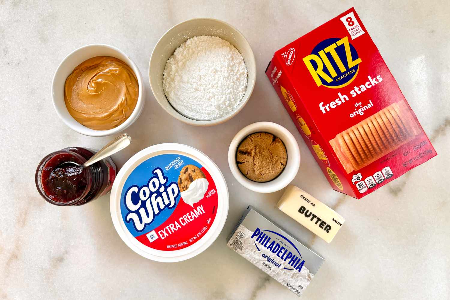 Ingredients on a counter including peanut butter powdered sugar Cool Whip cream cheese Ritz crackers butter and jam