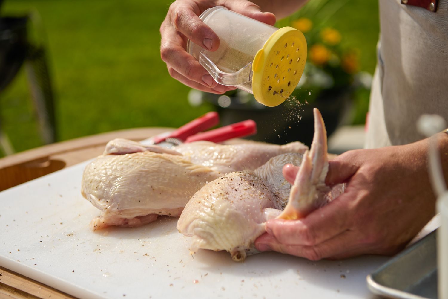 Seasoning raw chicken halves with spices on a white cutting surface, preparation for grilling for Grilled Half Chicken recipe
