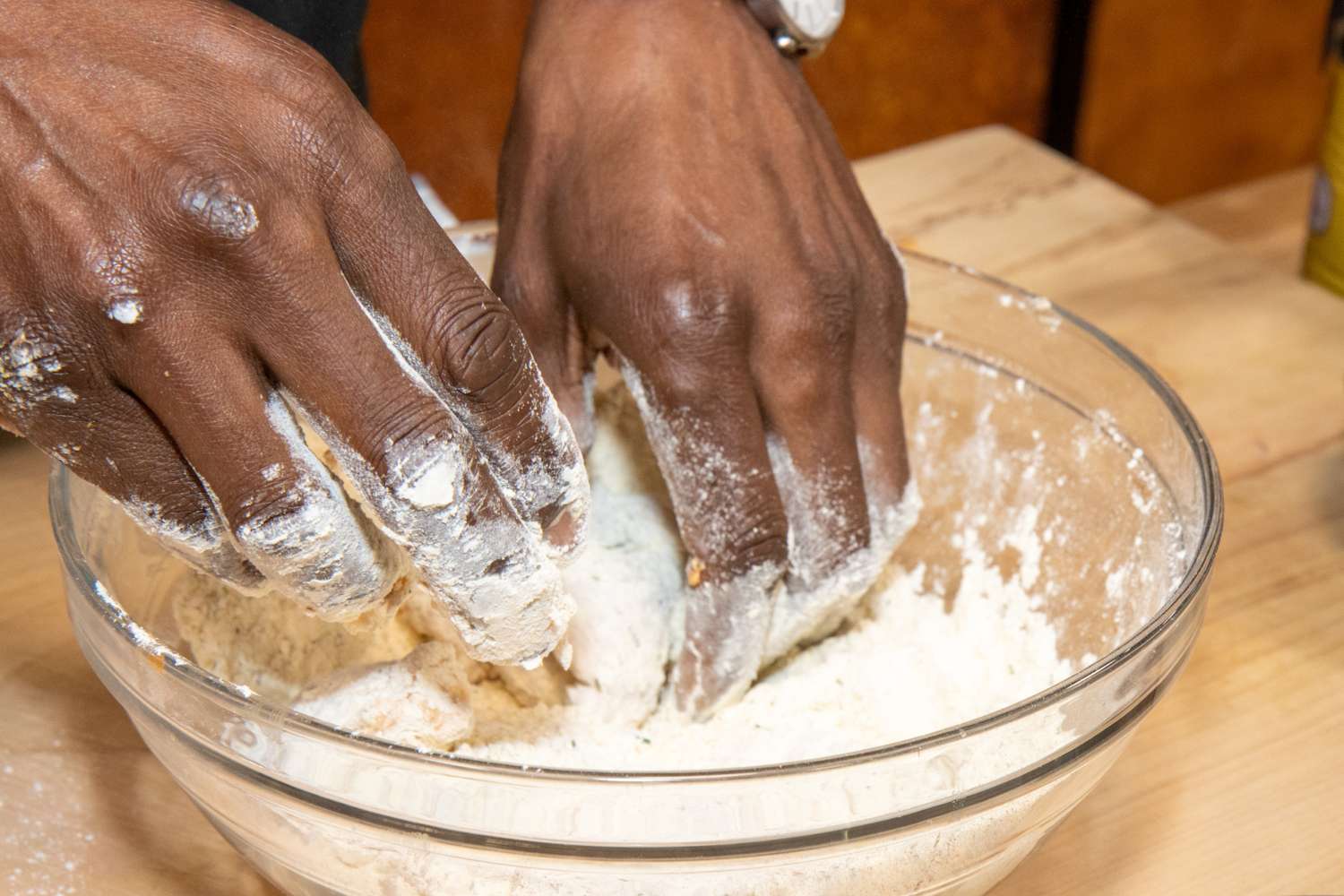 Hands coating chicken pieces with flour in a glass bowl