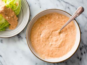 A bowl of Thousand Island Dressing with a spoon in it; a dressed wedge salad is to the side