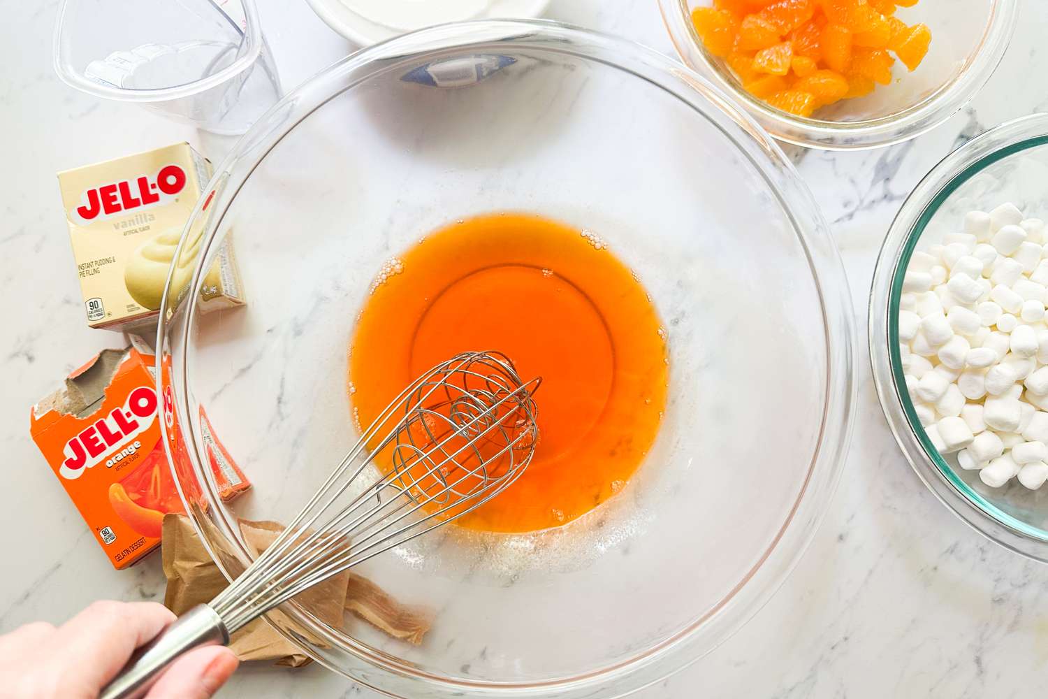 Ingredients for an orange creamsicle salad including gelatin and oranges in process with a whisk in a bowl