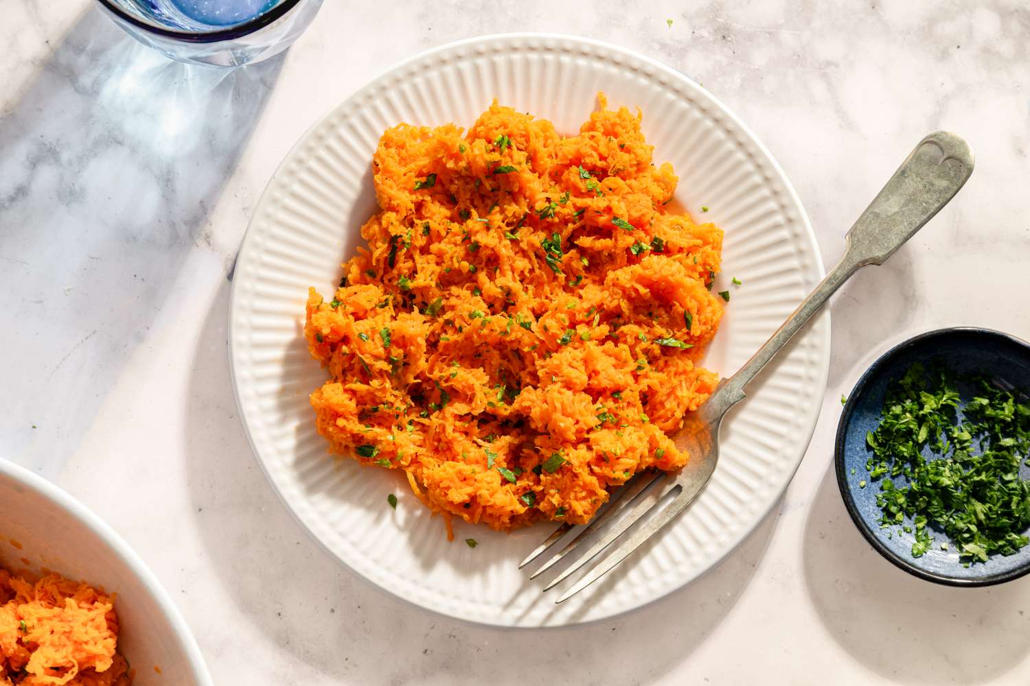Plate of shredded carrot salad with fork and garnish on side