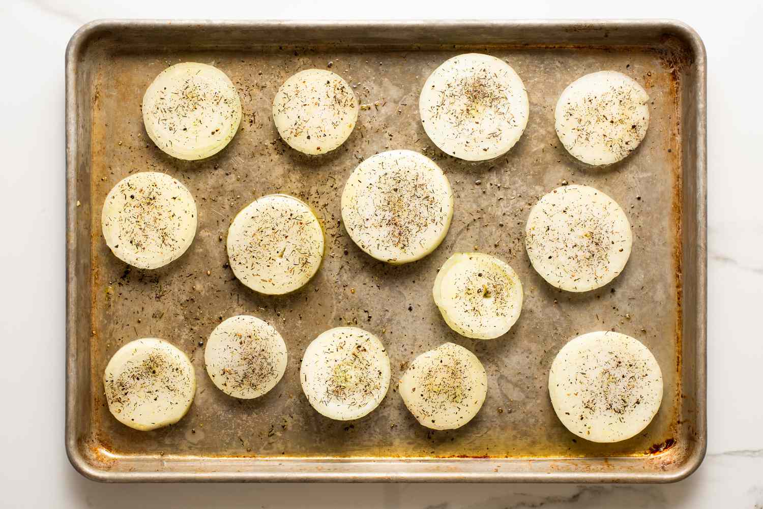overhead view of raw onions, oiled and seasoned on a sheet-pan for Melting Onions recipe