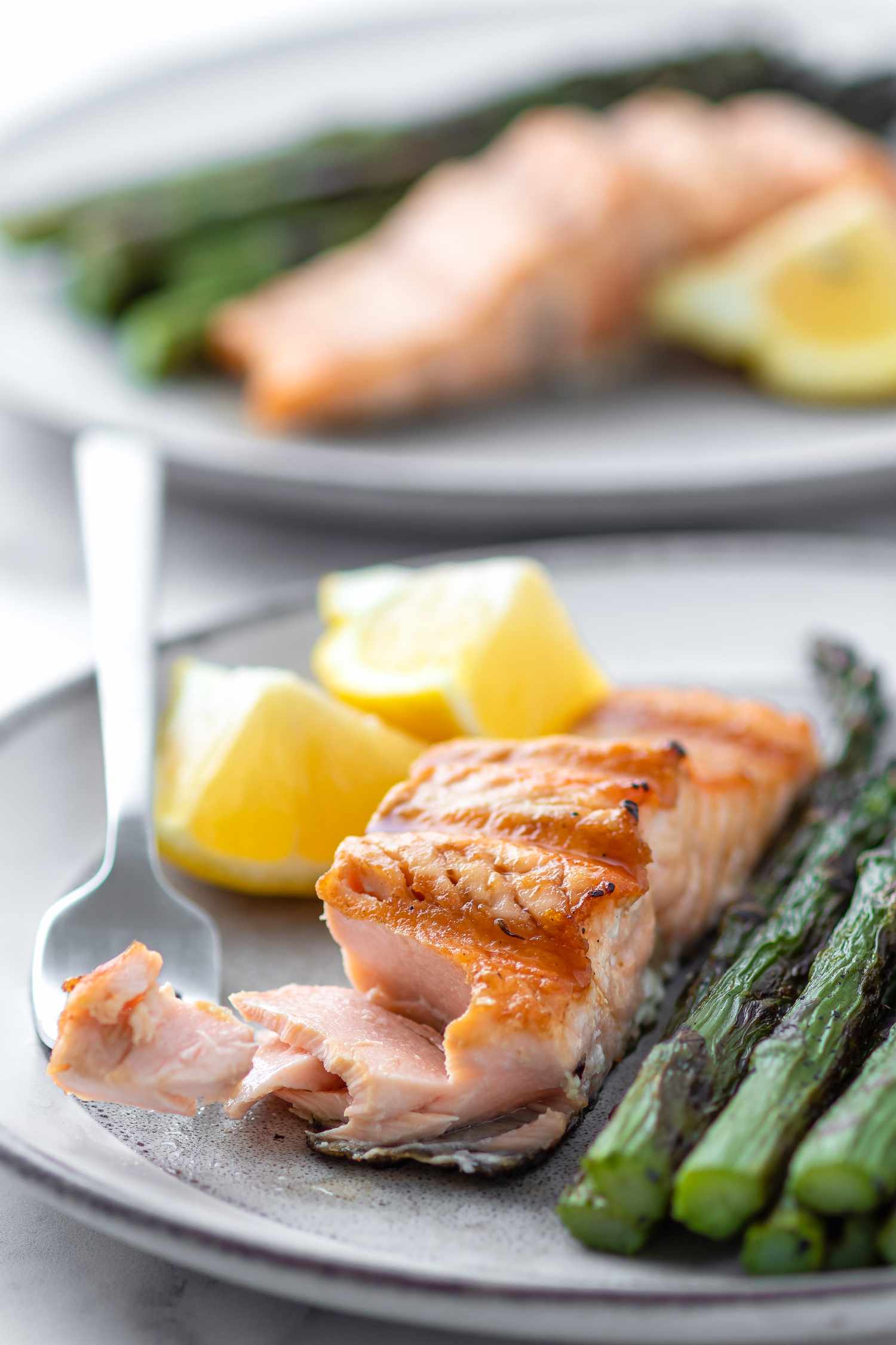Grilled salmon on a plate with asparagus and a second plate behind it.