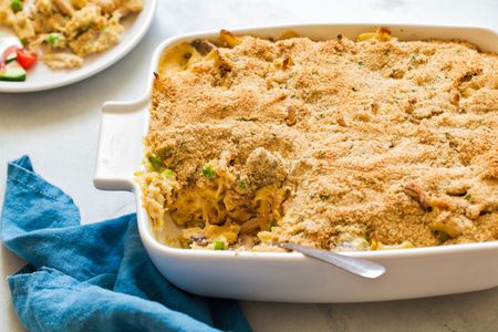 Angle view of a white baking dish of chicken tetrazzini with a slice removed next to a blue cloth napkin