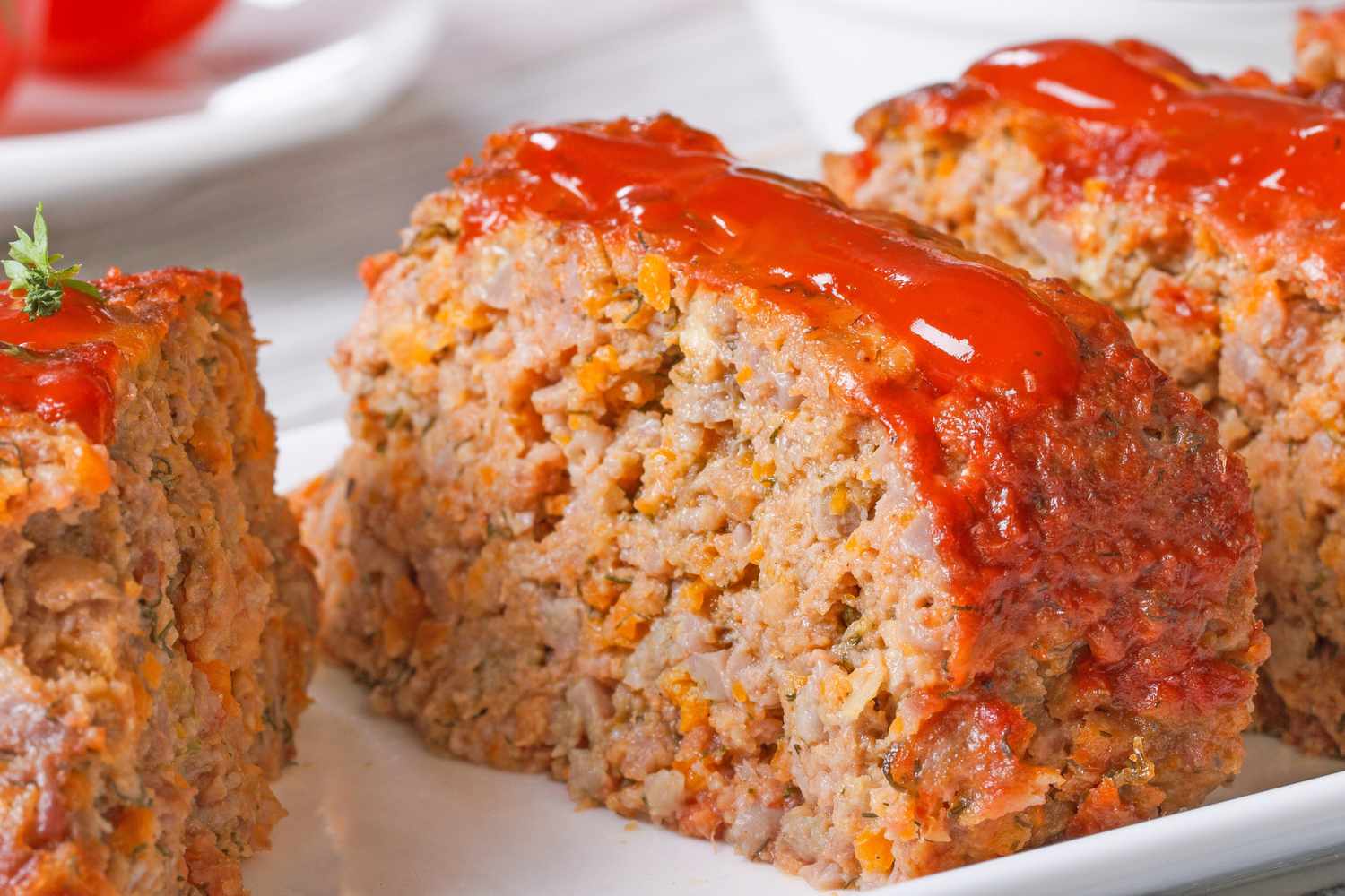 Slices of meatloaf topped with a layer of red sauce arranged on a plate
