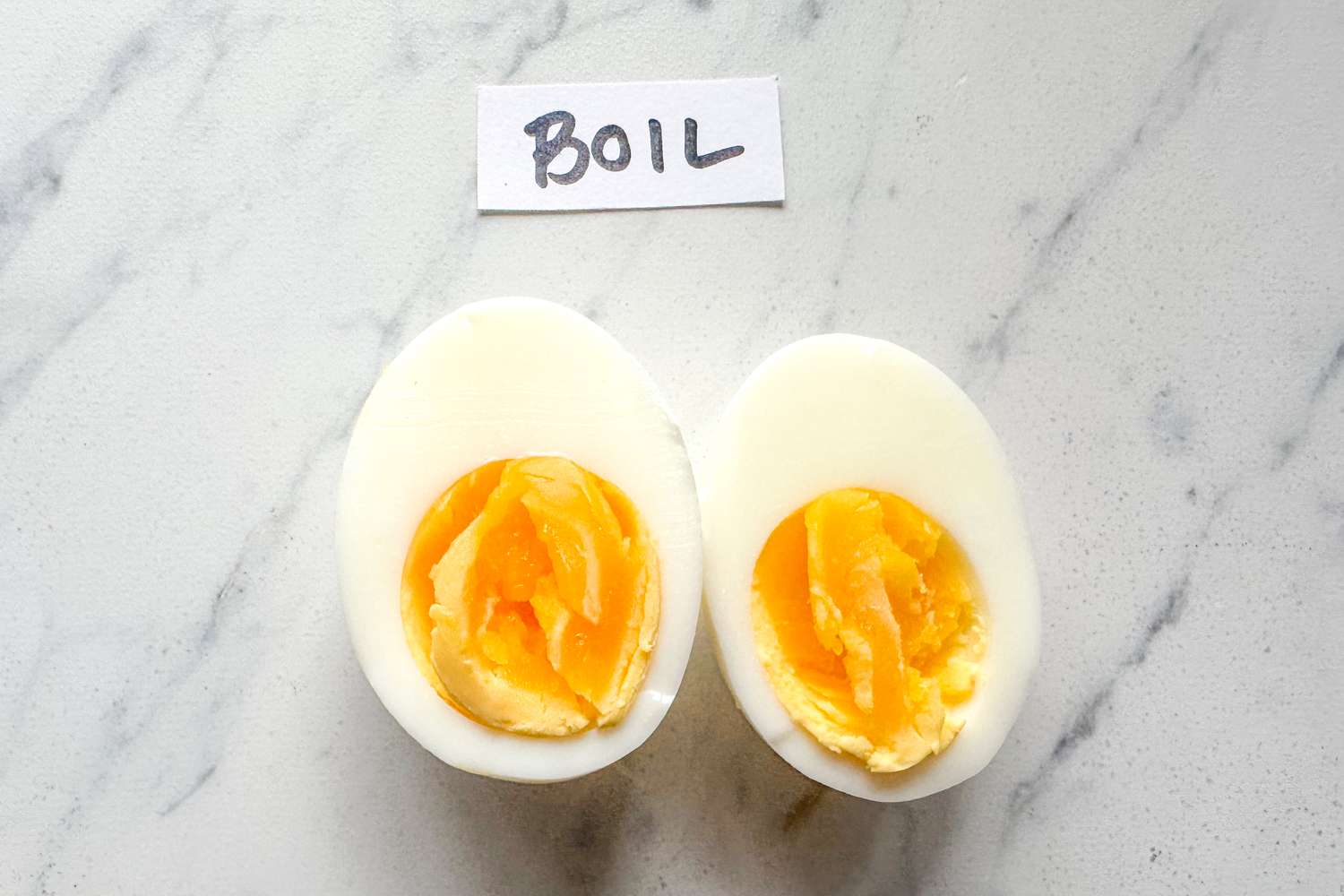 Two halved hardboiled eggs with a label reading Boil placed on a marble surface
