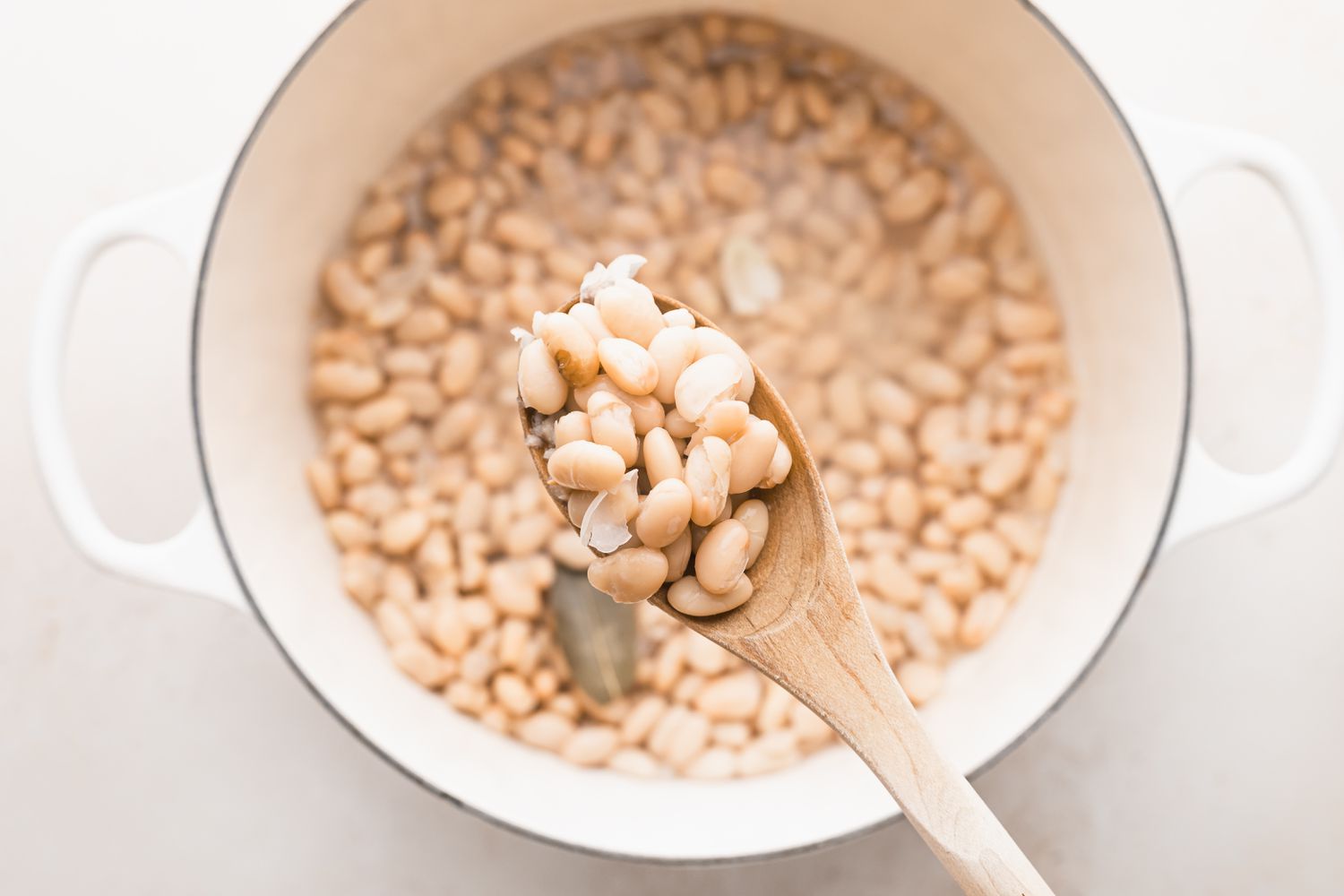 Spooning white beans out of a dutch oven to make white chicken chili.