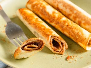 Three rolled cinnamon sugar tortillas on a plate with one cut in half, revealing the filling along a fork