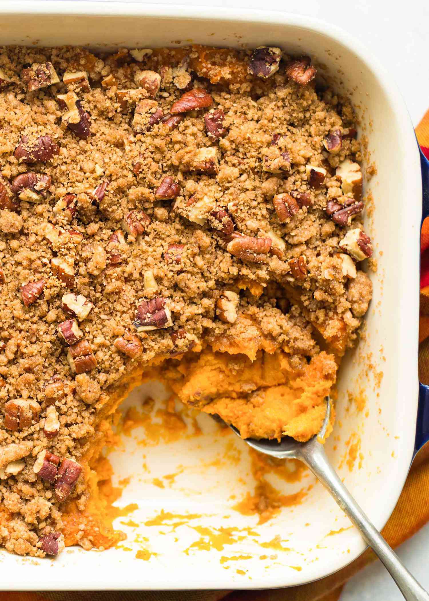 Sweet potato casserole with pecan crumb topping in a baking dish a serving spoon rests inside