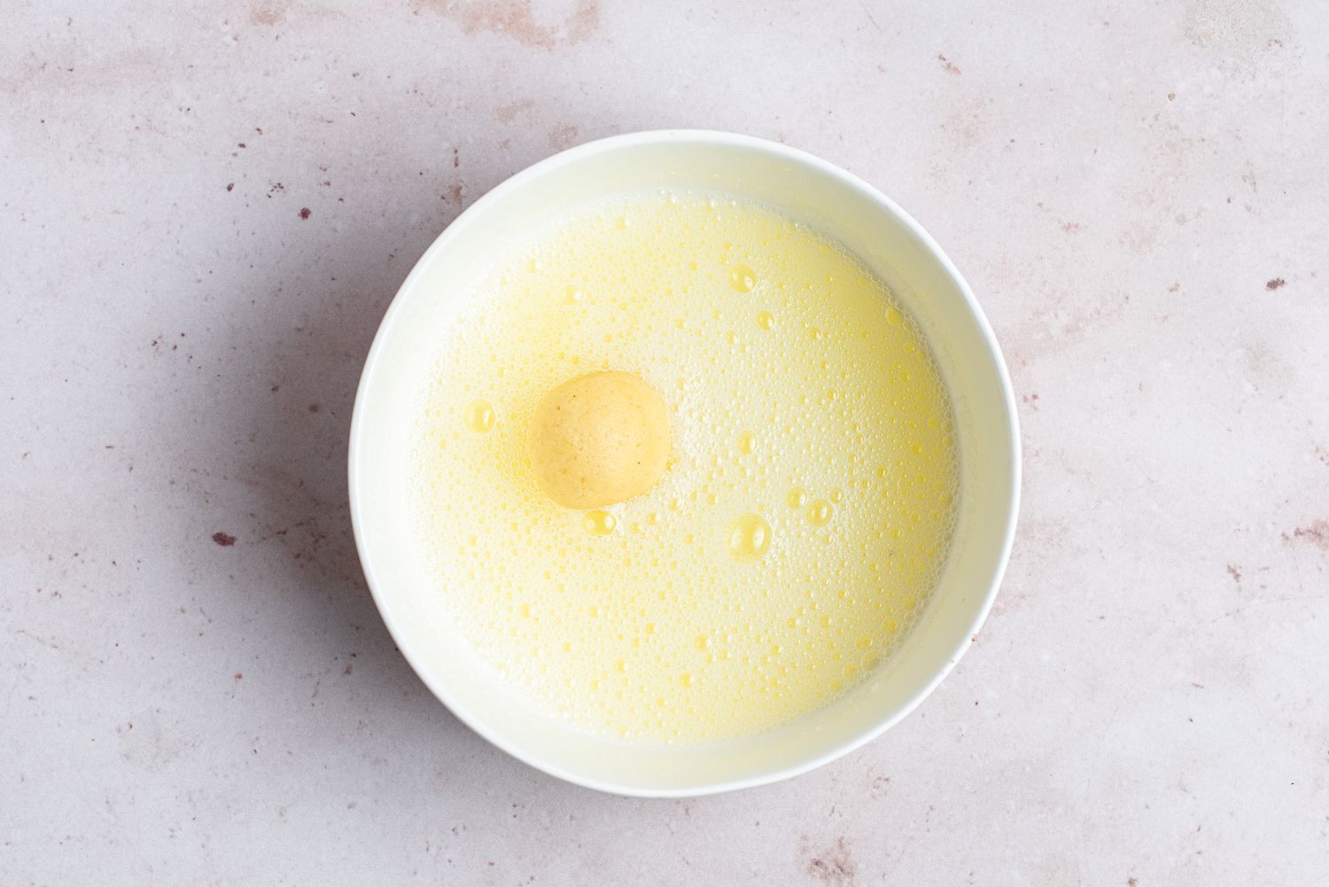 A dough ball being rolled in egg whites 