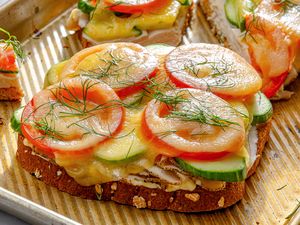 Openfaced sandwich with layers of sliced tomatoes cucumbers melted cheese and garnished with herbs served on a tray