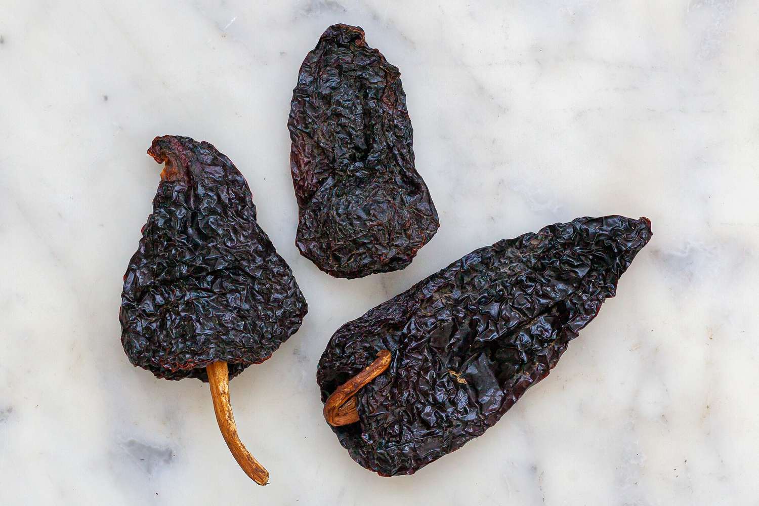 Three red chillis on a marble background.